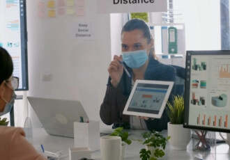 back-shot-business-womens-with-medical-face-mask-working-together-management-presentation-using-tablet-computer-while-sitting-company-office-team-respecting-social-distance (1)